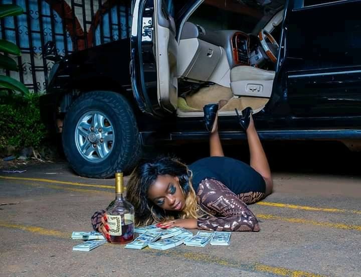 Angella Katatumba on the ground, legs on co-driver entrance with a Black Land cruiser in the background